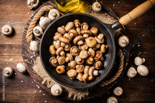 Frying pan with fried mushrooms on a wooden tray. 