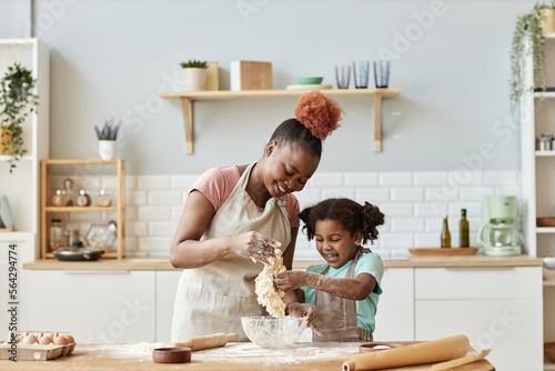 Happy black mother and daughter playing with dough baking together