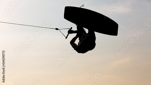 Silhouette Wakeboarder making tricks on sunset, Young surfer wakeboarding in the cable park, Extreme athlete having fun wakeboarding. photo