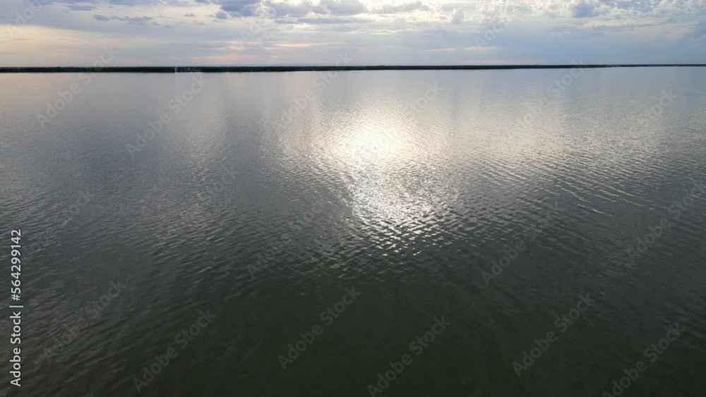 Aerial moving forwards close above a large lake with small waves under a cloudy blueish colored sky. A thin band of shoreline can be seen in the distance.
Aerial moving forwards close above a large lake with small waves under a cloudy blueish colored sky. A thin band of shoreline can be seen in the distance.