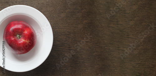 beautiful red apple in a white plate on a dark wooden surface, space for text