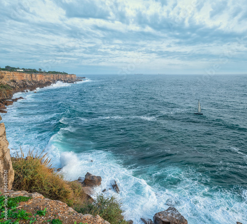 Beautiful cloudy sky and foaming waves approaching rocky shore of the Atlantic ocean. Beautiful nature background of Portugal.