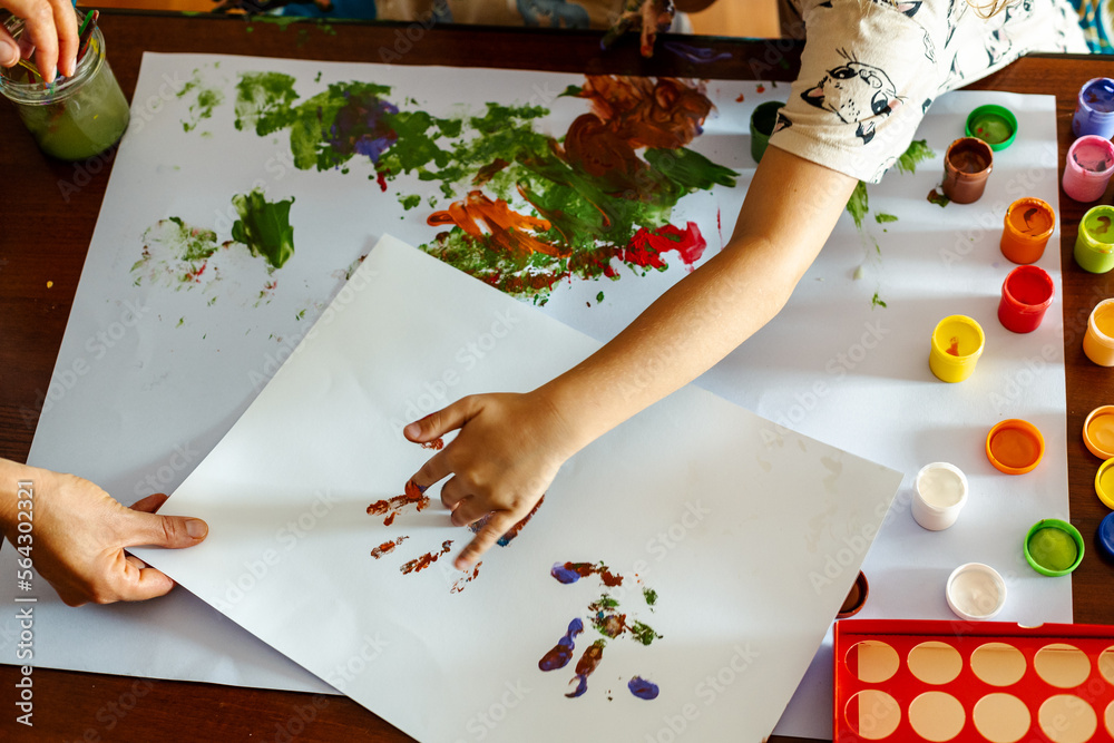 A little girl painting with her hands on a white sheet of paper.