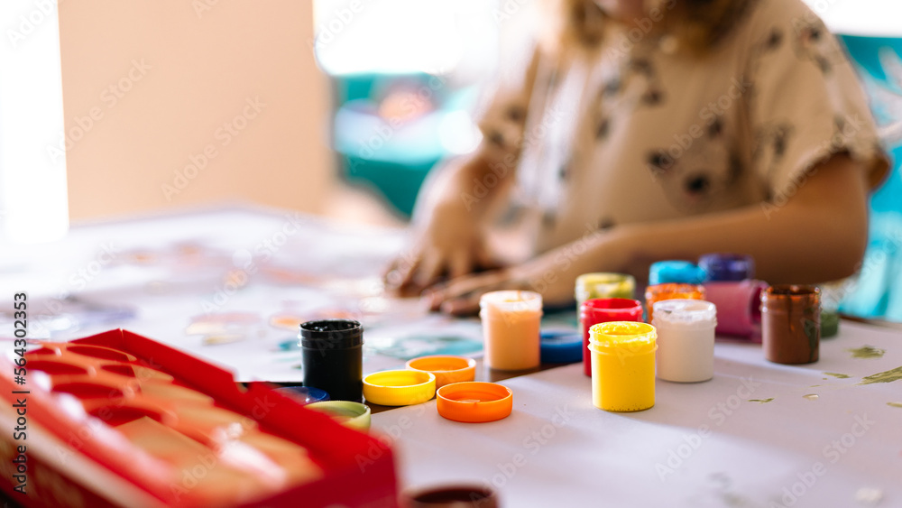 A little girl painting with her hands on a white sheet of paper.