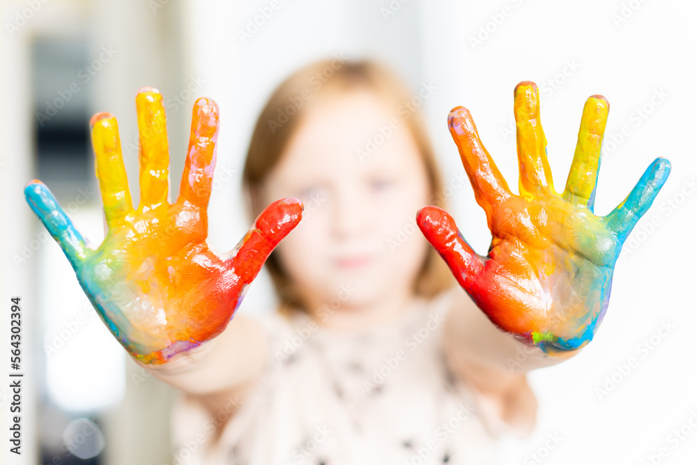 The little girl is showing her painted hands in rainbow colors.
