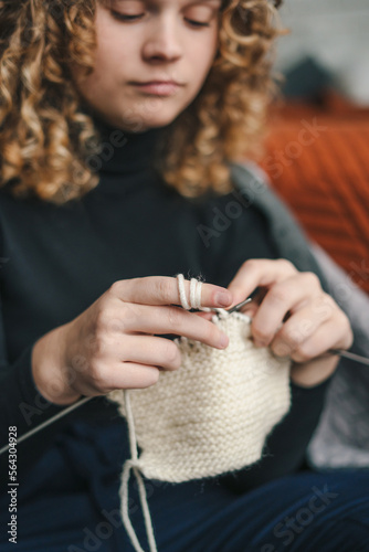 Head shot of a woman knitting at home, sitting on the floor in living room, happy positive enjoying leisure time, holding needles, hobby. Take break without