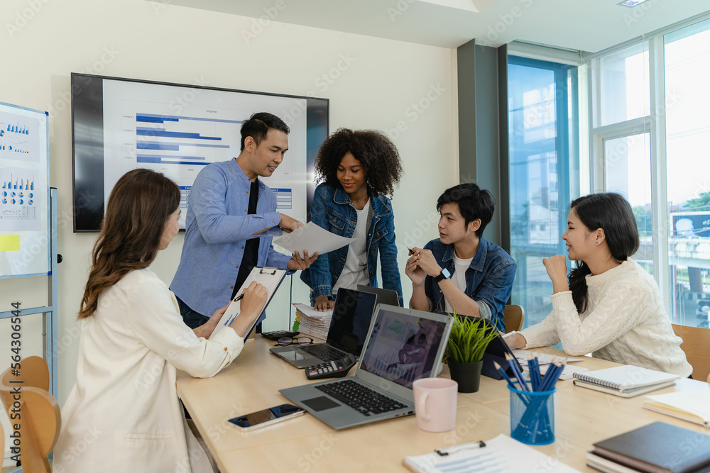 Group of Asian business people brainstorming at a meeting to start a new business. In a small office with a laptop and financial graphs on the table