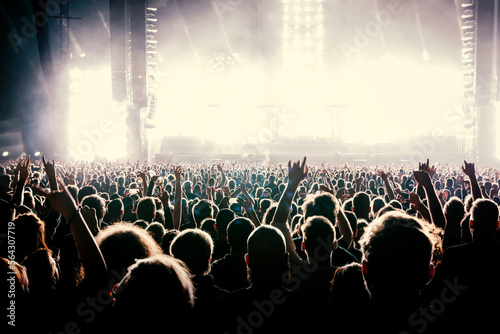 A crowd of people with raised arms during a music concert with an amazing light show. Black silhouettes