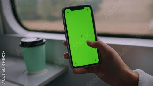 The hand of a woman holding a mobile phone with a green screen on the background of a train car