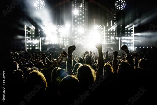 A crowd of people with raised arms during a music concert with an amazing light show. Black silhouettes