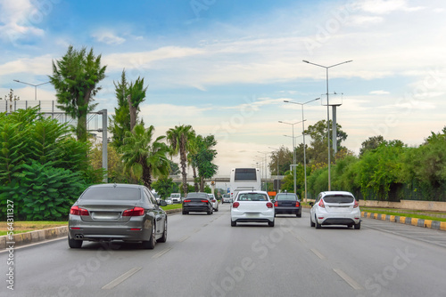Dense stream of cars on a city road back view, a green street. © aapsky