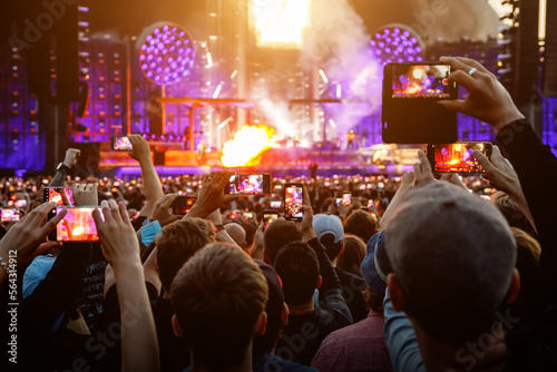 Hand with a smartphone record live music festival and taking photos of the concert. © 9parusnikov