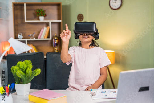 Girl kid with vr or virtual head set listening online or virtual class in front of study table at home - conecept of modern education, learning and technology