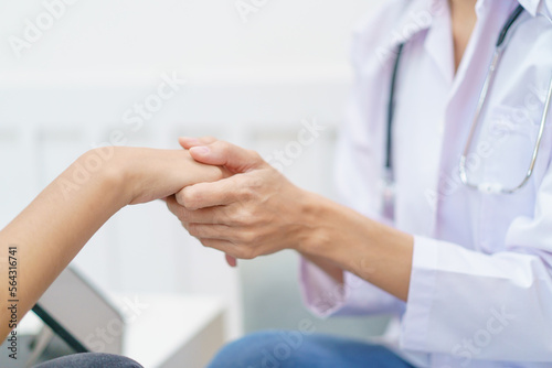 Female specialist or professional doctor giving a consulting to female patient in clinic. Doctor touching or holding on crisis patient's hand with empathy and care.