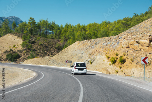 White car on a turn in rocky arid mountains with coniferous trees.
