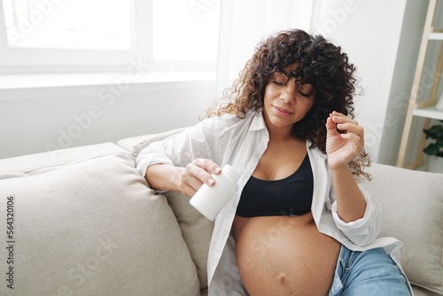 Pregnant woman smile blogger takes vitamins sitting on the couch at home freelancer in the last month of pregnancy lifestyle before childbirth