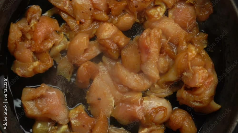 A wooden spoon moves chicken fillet pieces 