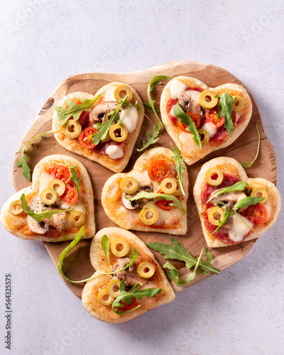 Heart shape mini pizzas on wooden board for Valentines day holiday, top view