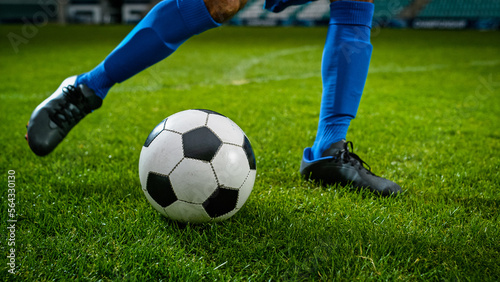 Close-up of a Leg in a Boot Kicking Football Ball. Professional Soccer Player Hits Ball with Fierce Power, Scores Goal, Grass Flying. Football Championship Concept. Low Angle Ground Artistic Shot