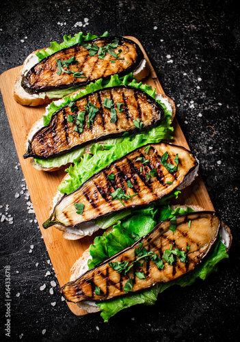 Sandwich with grilled eggplant and lettuce on a wooden cutting board. 