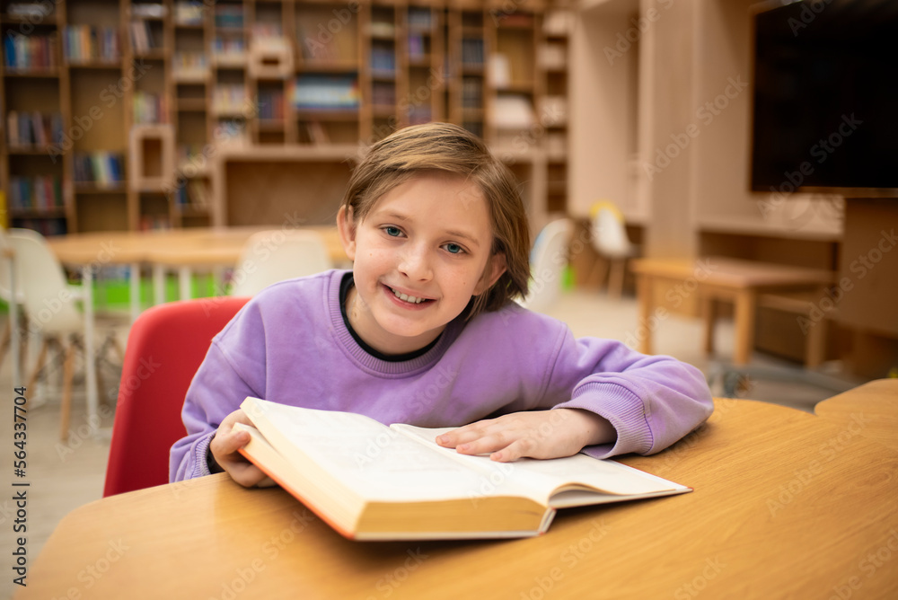boy reading a book, doing homework while sitting at a table in a classroom or library boy reading a book, doing homework while sitting at a table in a classroom or library