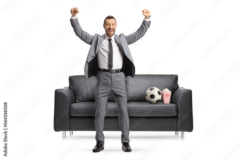 Excited businessman cheering in front of a black sofa with a football Excited businessman cheering in front of a black sofa with a football