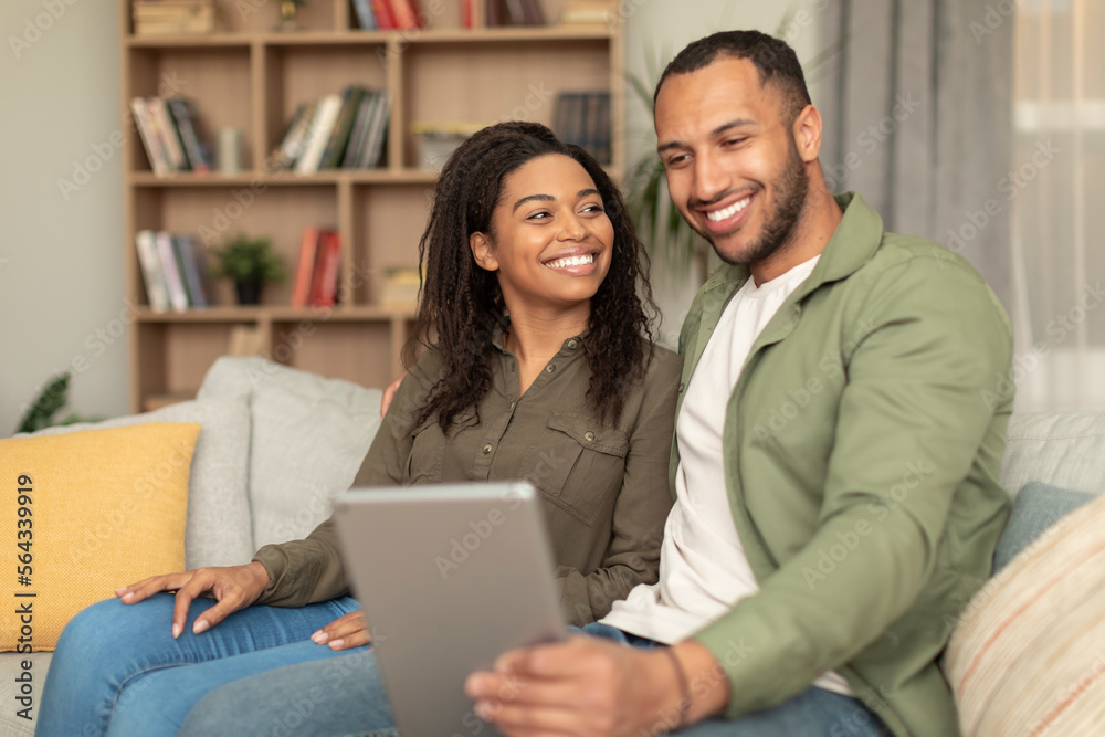 Happy black lovers sitting on couch and using digital tablet, having video call or surfing internet, copy space Happy black lovers sitting on couch and using digital tablet, having video call or surfing internet, copy space