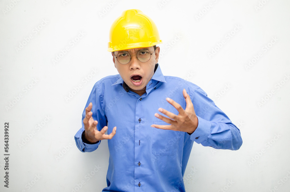 asian male construction worker or engineer in blue shirt and safety yellow helmet shows expresion of anger, furious and dissapointment isolated over white. stressed over work concept