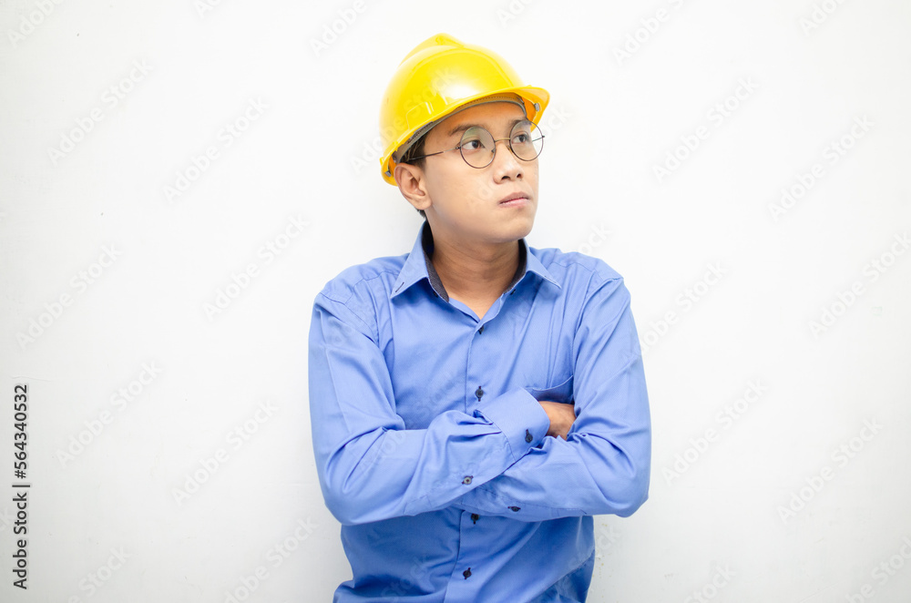Asian construction worker in blue shirt and yellow safety helmet is seriously thinking with a wondering and thinking gesture and expression. Asian construction worker in blue shirt and yellow safety helmet is seriously thinking with a wondering and thinking gesture and expression.
