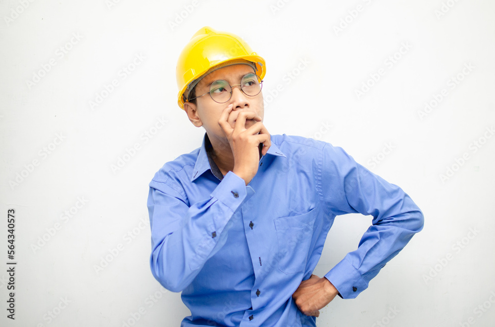 Asian construction worker in blue shirt and yellow safety helmet is seriously thinking with a wondering and thinking gesture and expression. Asian construction worker in blue shirt and yellow safety helmet is seriously thinking with a wondering and thinking gesture and expression.