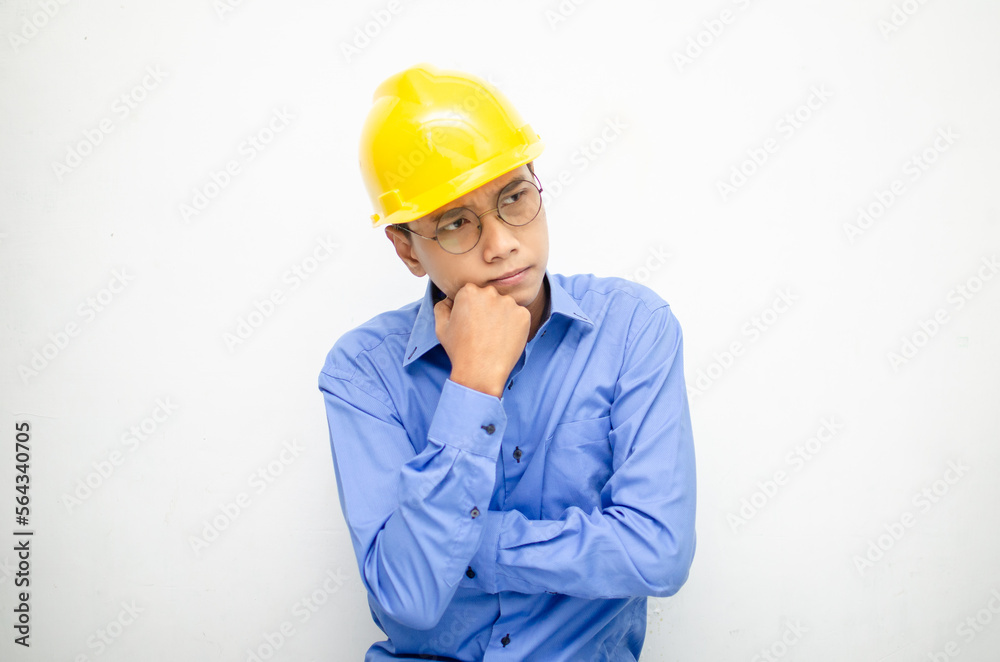 Asian construction worker in blue shirt and yellow safety helmet is seriously thinking with a wondering and thinking gesture and expression. Asian construction worker in blue shirt and yellow safety helmet is seriously thinking with a wondering and thinking gesture and expression.