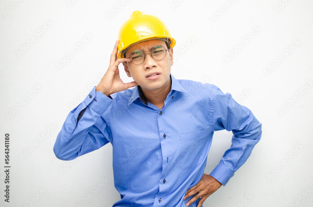 asian male construction worker or engineer in blue shirt and safety yellow helmet shows expresion of anger, furious and dissapointment isolated over white. stressed over work concept asian male construction worker or engineer in blue shirt and safety yellow helmet shows expresion of anger, furious and dissapointment isolated over white. stressed over work concept