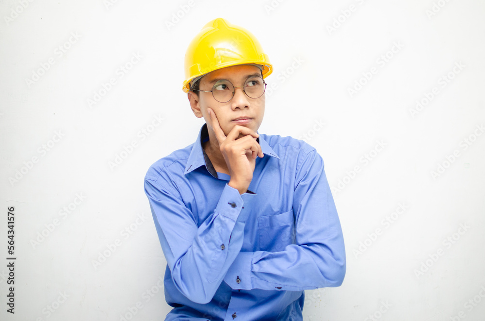 Asian construction worker in blue shirt and yellow safety helmet is seriously thinking with a wondering and thinking gesture and expression. Asian construction worker in blue shirt and yellow safety helmet is seriously thinking with a wondering and thinking gesture and expression.