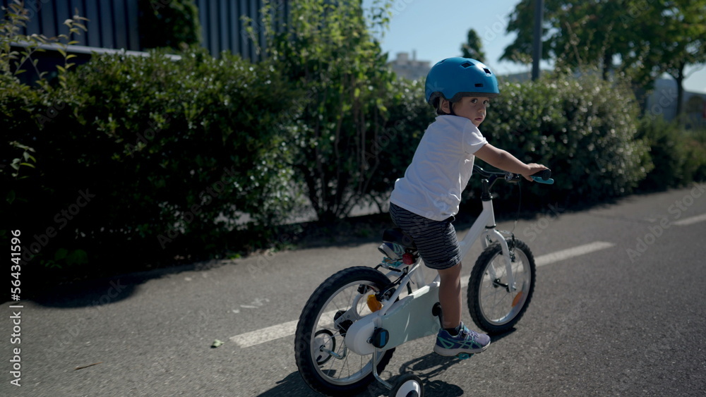 Active little boy rides bicycle outside wearing helmet on green road