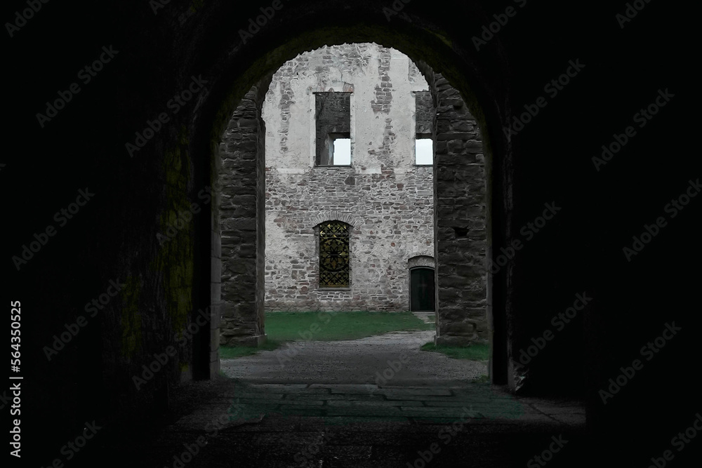 Exit from inside a castle. Arched opening with ancient walls. Military fort, medieval castle. Internal garden and ancient architecture.