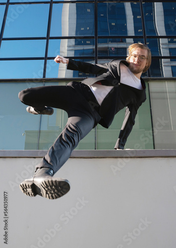businessman jumping doing parkour with long blonde hair and glasses executive business clothes