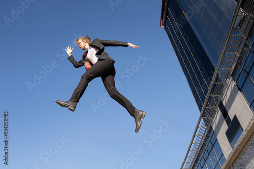 businessman jumping doing parkour with long blonde hair and glasses executive business clothes