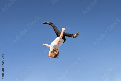 caucasian blond boy doing a backflip and parkour with blue sky in the background photo