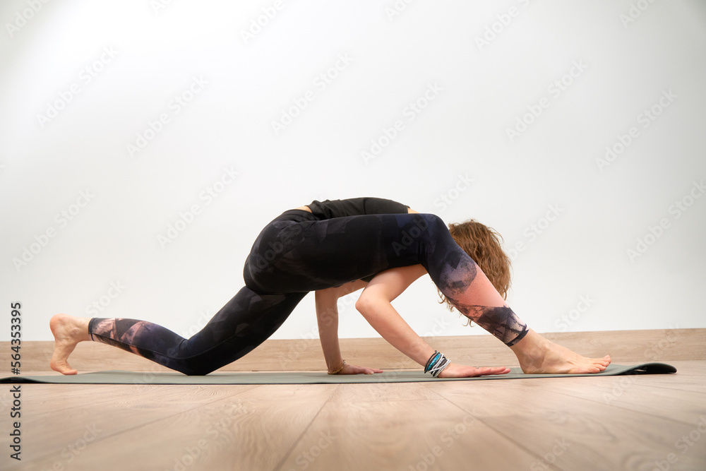 Young and sporty girl doing exercise on gray mat. Confident beautiful woman does yoga exercises in a modern sport center. Health concept. Purposeful girl trying to perform a complex exercise.