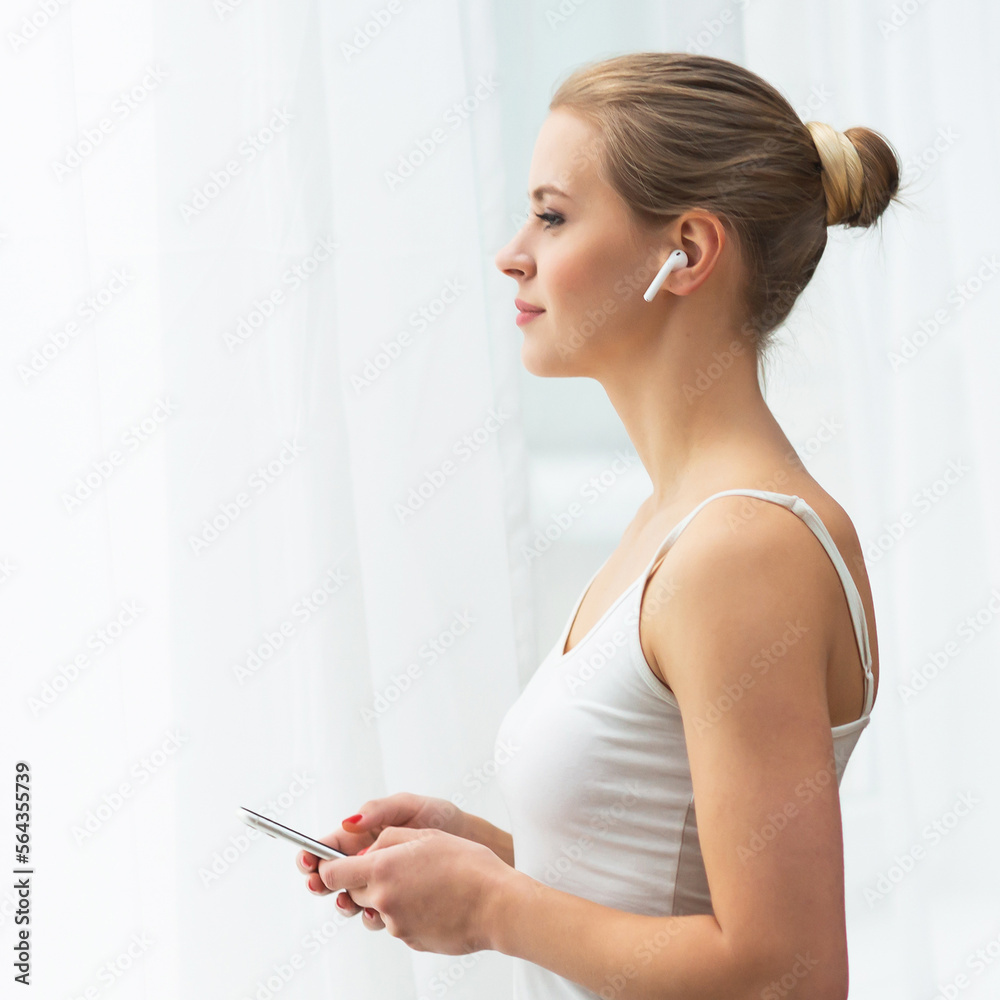 Young woman in white underwear is standing in front of the window and looking into it. Girl at home in the living room. Young woman in white underwear is standing in front of the window and looking into it. Girl at home in the living room.