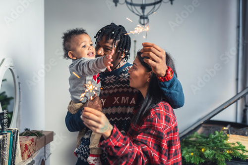 Smiling multicultural parents and their toddler with Christmas sparkling fire sticks. High quality photo