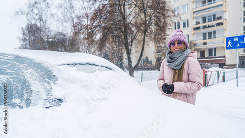 Woman in sunglasses standing next to the car burried under the snow . High quality photo