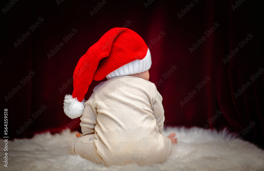 Cute baby in a Santa hat. Christmas mood and new year on a burgundy background. Copy space