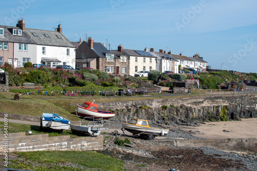 Boats in the rocky bay at fishing village Craster in Northumberland, UK. Against a backdrop of a row of cottages photo