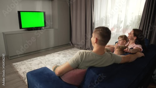 Lifestyle happy family watching TV together in the living room. Parents and children are sitting on the sofa and smiling, watching cartoons on television. High quality 4k footage