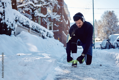 Male athlete tying shoelace while working out outdoors in snow.