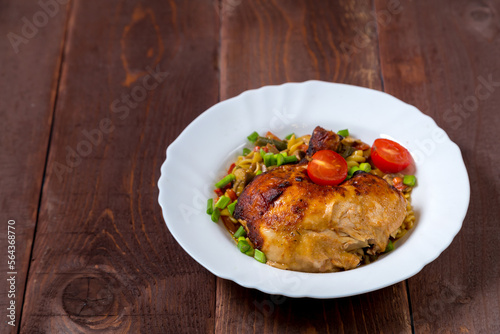 Pasta with vegetables and baked chicken leg sprinkled with green onions in a plate on a wooden table.copy space