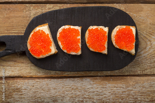 Toasts with red caviar and butter on a black handmade board on a wooden table.