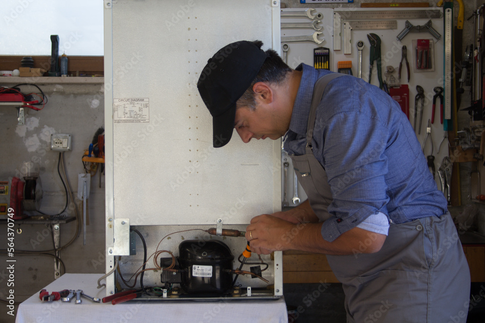 Image of a handyman technician in his workshop repairing a refrigerator motor. Image of a handyman technician in his workshop repairing a refrigerator motor.