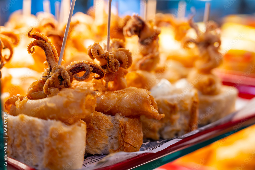 Fototapeta premium Typical snack of Basque Country, pinchos or pinxtos skewers with small pieces of bread, sea food, baby octopus, cheese, jamon served in bar in San-Sebastian or Bilbao, Spain